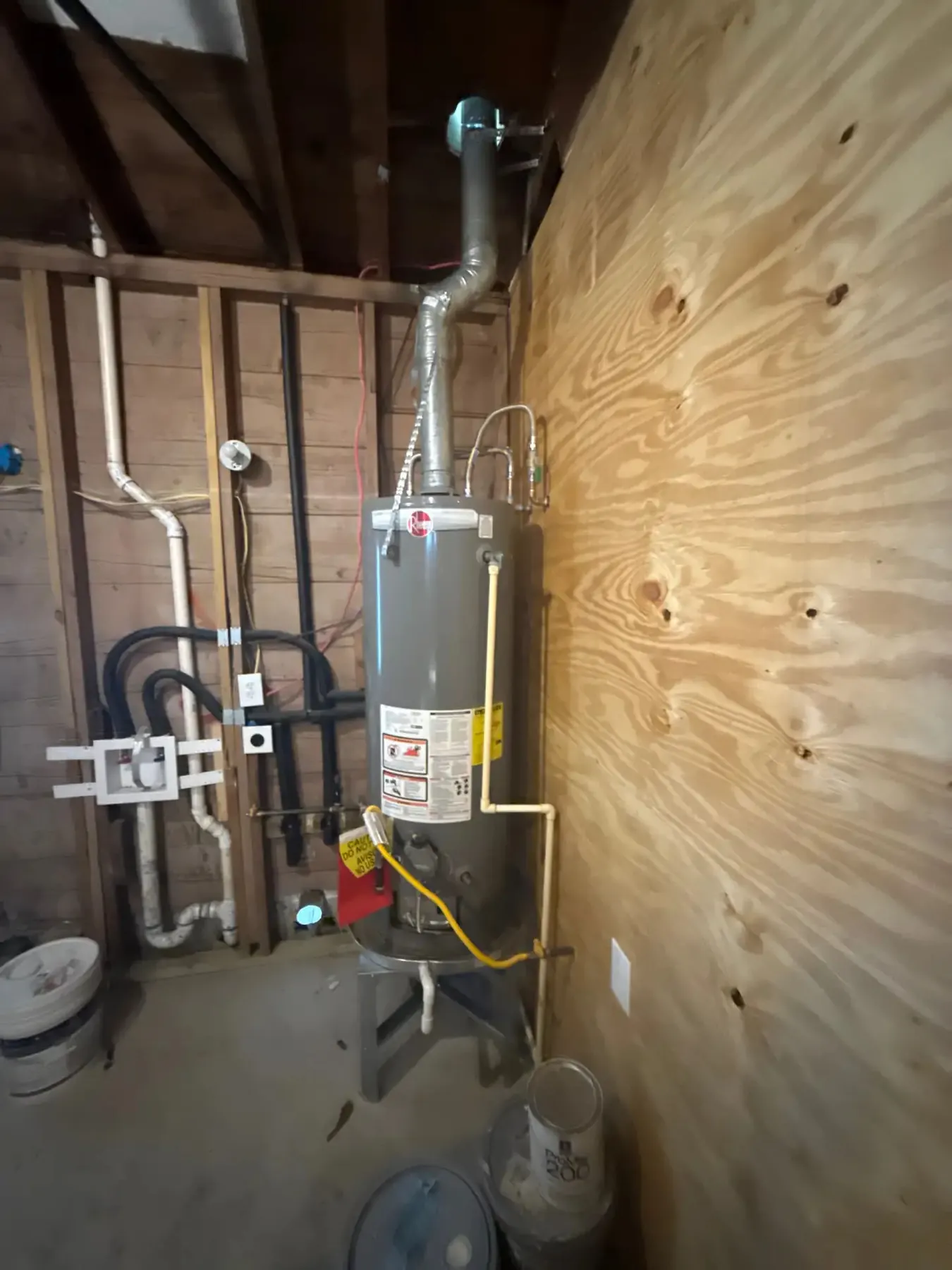 Residential water heater installed in a basement, with the connected plumbing clearly visible.