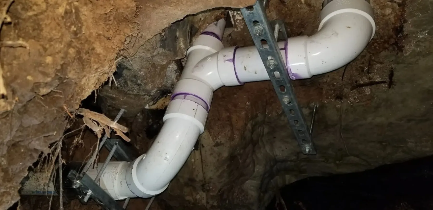 Underground plumbing with white PVC pipes and supports in an open trench.