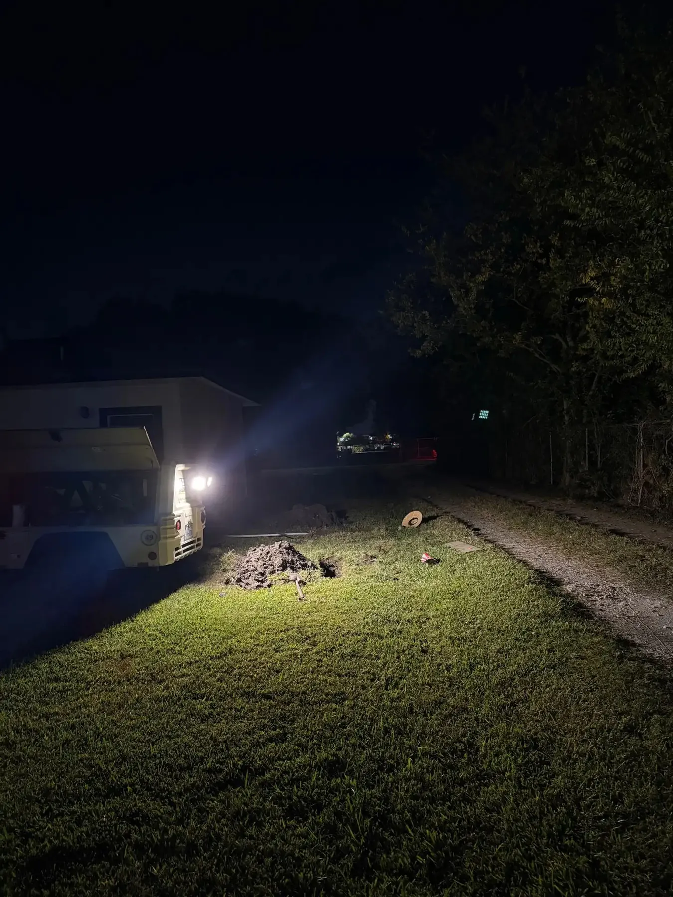 Evening excavation work with a lit access path and a service vehicle nearby.