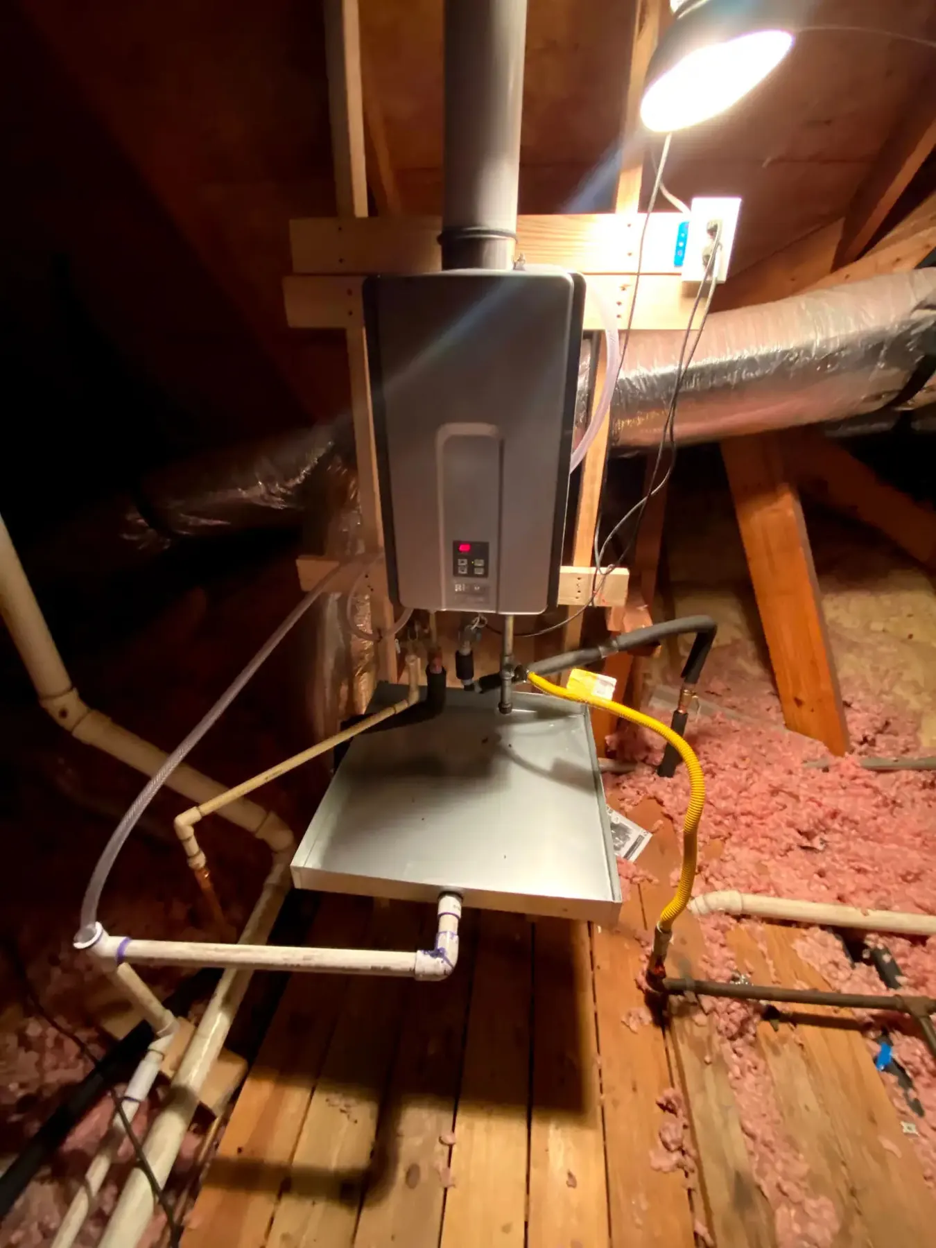 Tankless water heater connected to exposed attic pipework.