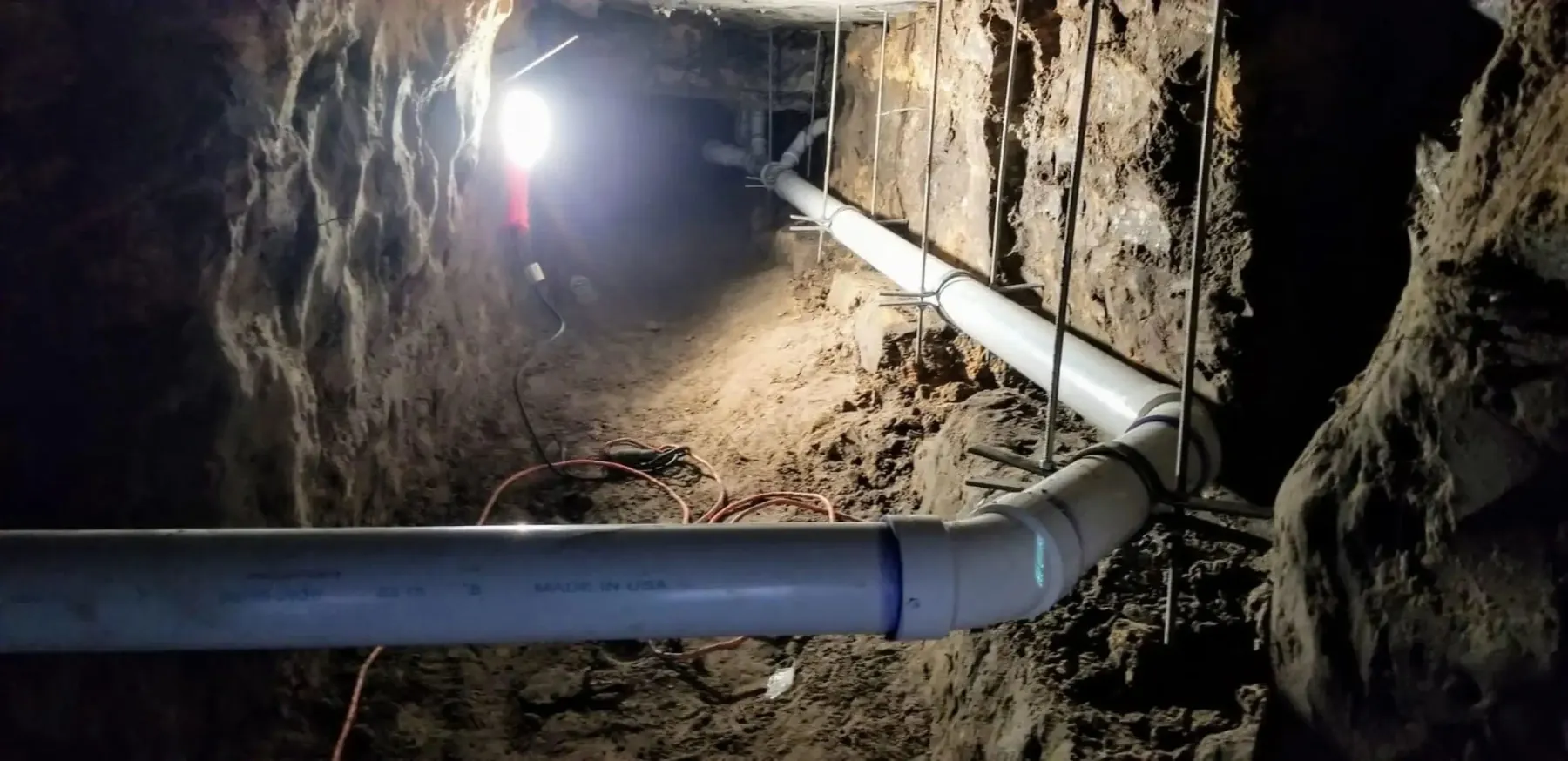 Underground tunnel with PVC pipes surrounded by excavated earth.