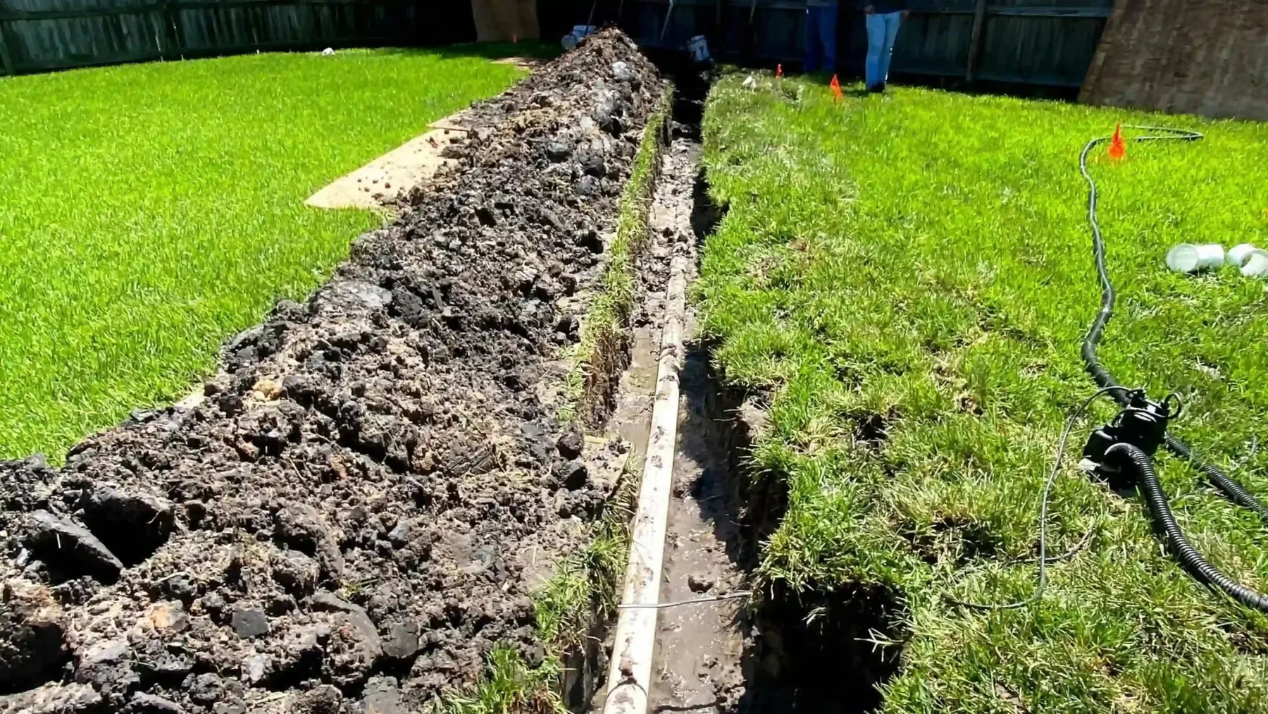 Excavated trench across a grassy yard for underground plumbing access.