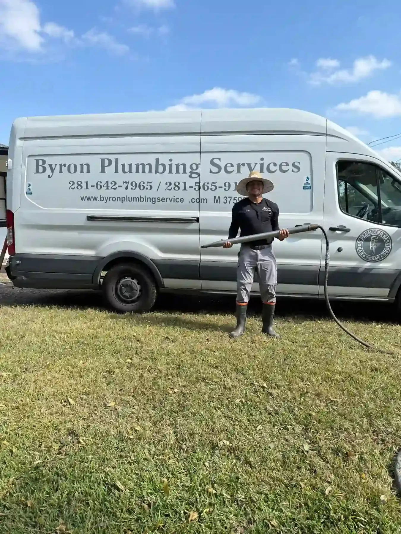 Plumber holding a service hose beside a Byron Plumbing Services van.