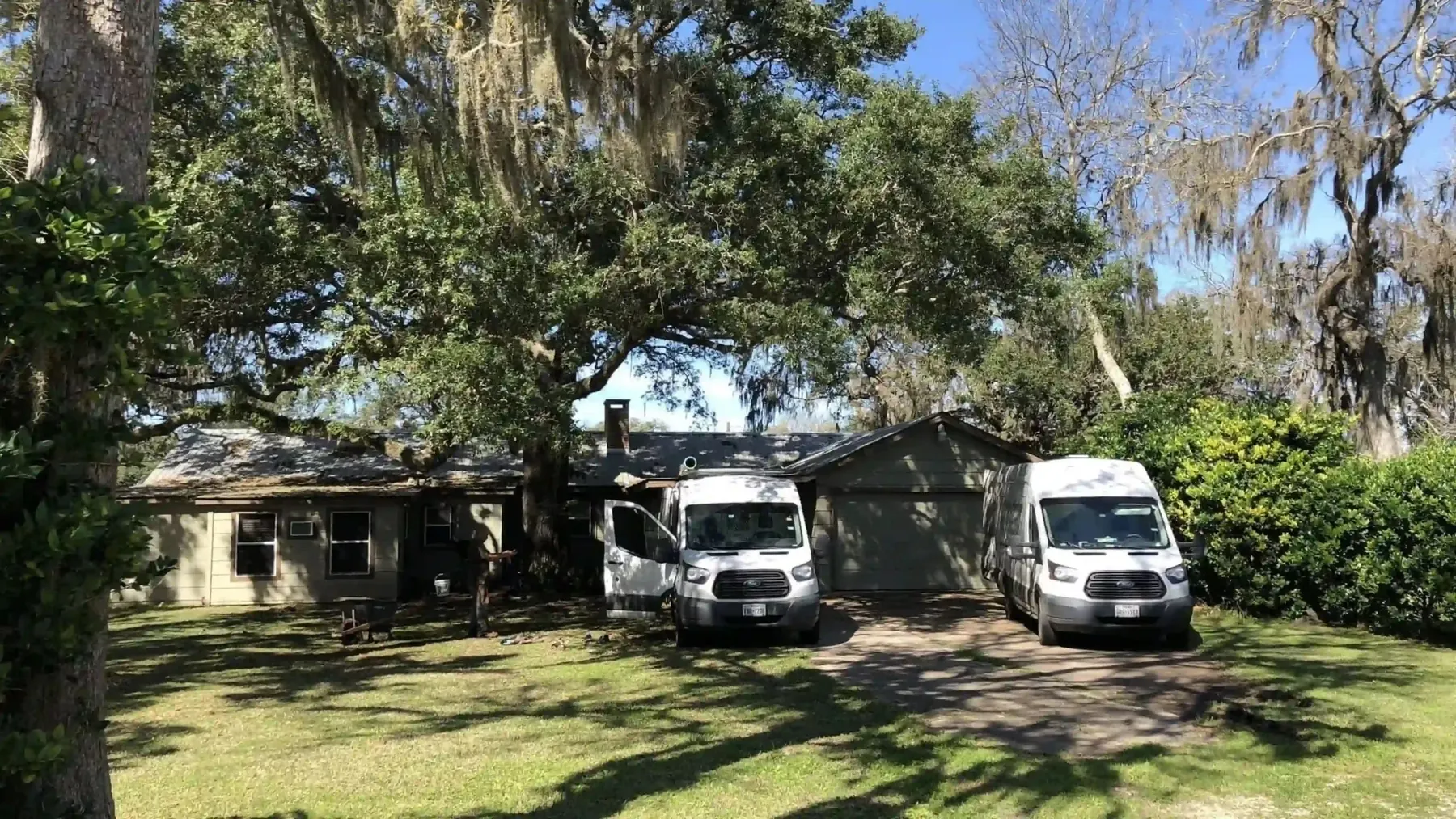 Two Byron Plumbing Services vans parked at a home beneath a large tree.